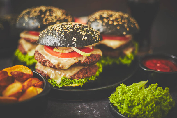 Hamburgers noirs appétissants et pommes de terre frites - Photo, image