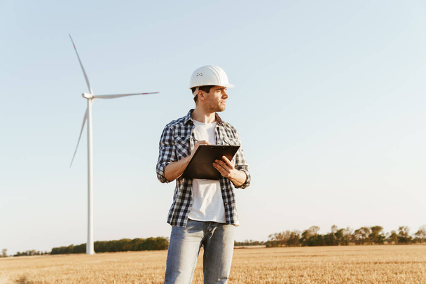 An electrical engineer standing on a field with windmills, taking notes - Foto, immagini