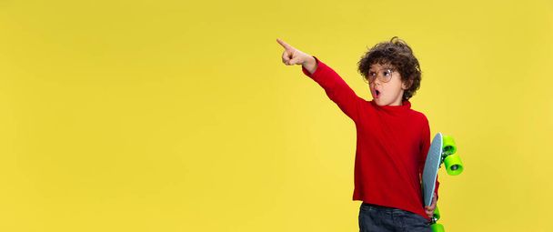 Pretty young curly boy in red wear on yellow studio background. Childhood, expression, fun. - Фото, зображення