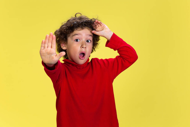 Pretty young curly boy in red wear on yellow studio background. Childhood, expression, fun. - Fotoğraf, Görsel