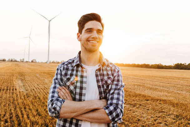 Hombre feliz de pie contra el paisaje industrial con turbinas eólicas - Foto, imagen