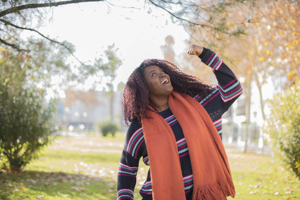 beautiful African American woman with long hair wearing colorful sweater showing  fist     in autumn  park   - Foto, afbeelding