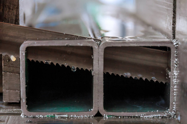 Corte de perfiles y tuberías de acero en una sierra de cinta en producción. - Foto, imagen