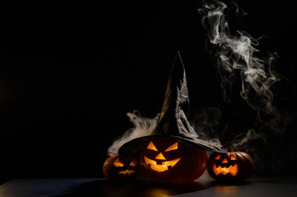 Three jack o lanterns glow in the dark amidst the fog. Halloween pumpkin in a witch hat. - Foto, imagen
