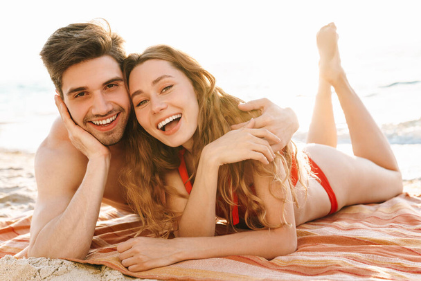 Νεαρό ευτυχισμένο ζευγάρι στην παραλία, ξαπλωμένο στην άμμο - Φωτογραφία, εικόνα