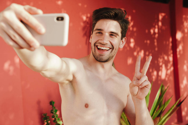 Happy young shirtless man taking a selfie on the beach - Fotografie, Obrázek