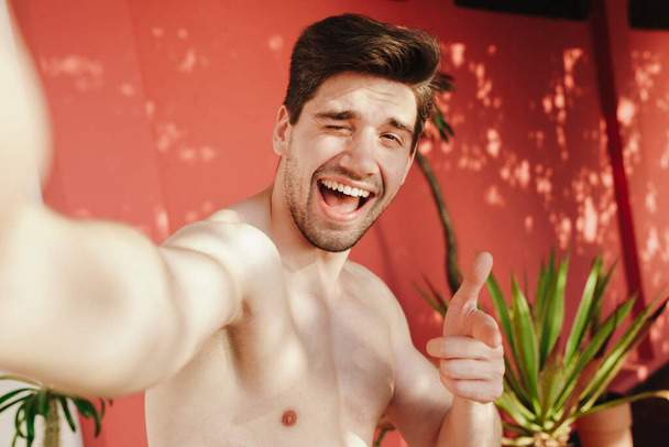 Happy young shirtless man taking a selfie on the beach - Фото, изображение