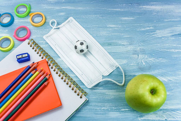 Школьные принадлежности на синем фоне. Возьми медицинскую маску в школу. take a snack to school like an apple - Фото, изображение
