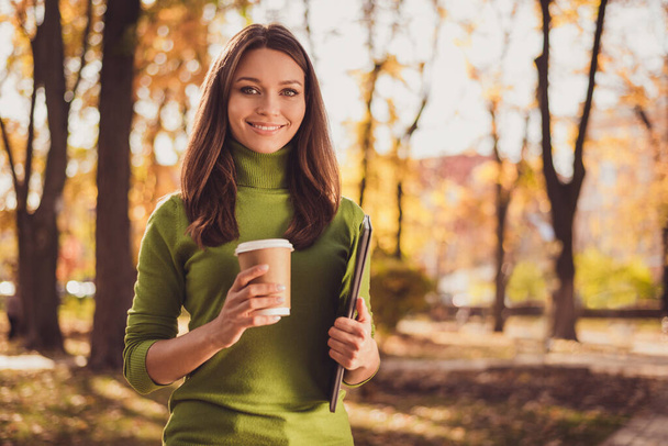 Photo of cute lovely lady stay hold laptop drink coffee beaming toothy smiling make stop enjoy autumn park trees beautiful atmosphere wear green turtleneck orange pants outdoors - Фото, изображение