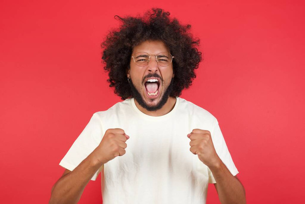 Young man with afro hair    is angry   against red  wall  - Foto, Imagem