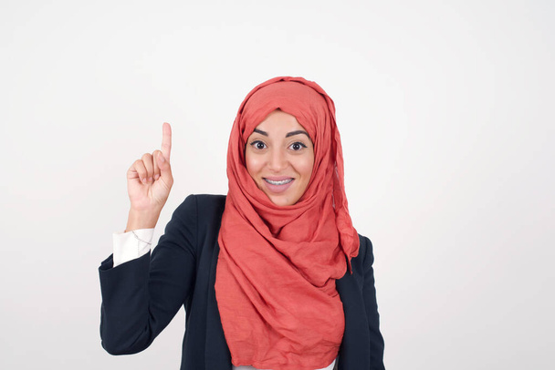 Close-up portret van charmante Mooie moslim vrouw draagt zwarte blazer en hijab in casual kleding wijzen met een vinger omhoog, omhoog kijken en glimlachen, Ik heb een idee, Ik weet het antwoord of de oplossing. - Foto, afbeelding