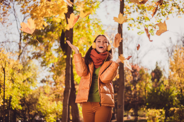 Photo of pretty lovely lady beaming smiling throwing yellowed falling leaves stay among maples city park wear headphones scarf green turtleneck orange windbreaker pants outdoors - Foto, Imagen