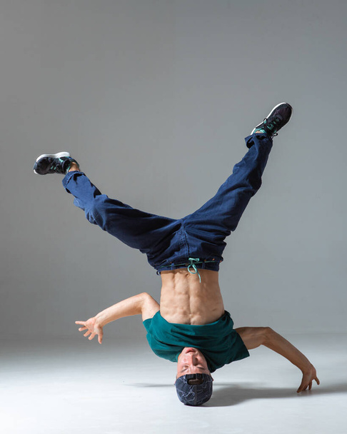 Stylish guy dancer dancing on head breakdance in studio isolated on gray background. Breakdance lessons - Foto, Imagen