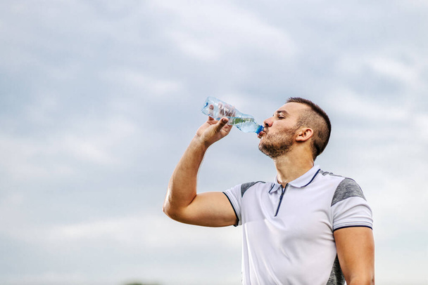 Vermoeide dorstige voetballer op vorm neemt een pauze en drinkwater. - Foto, afbeelding