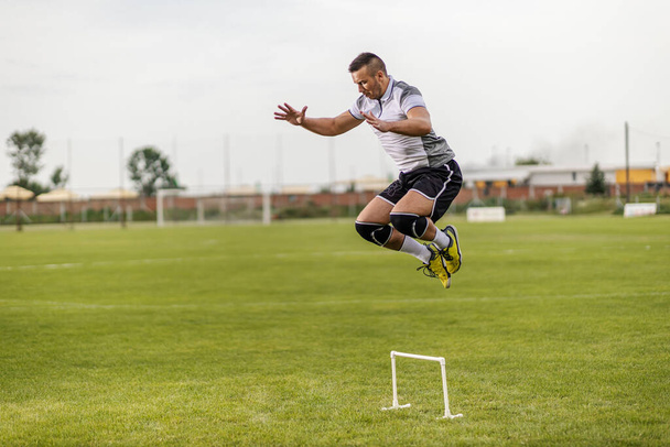 Dedicado forte atraente jogador de futebol ajuste pulando sobre obstáculo. - Foto, Imagem