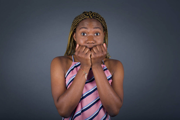 mooi jong Afrikaans amerikaans vrouw bedekken haar mond met haar handen terwijl staan op grijs achtergrond - Foto, afbeelding