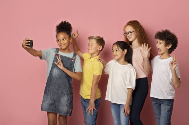 Багатонаціональні школярі беруть селфі разом на рожевий фон
 - Фото, зображення