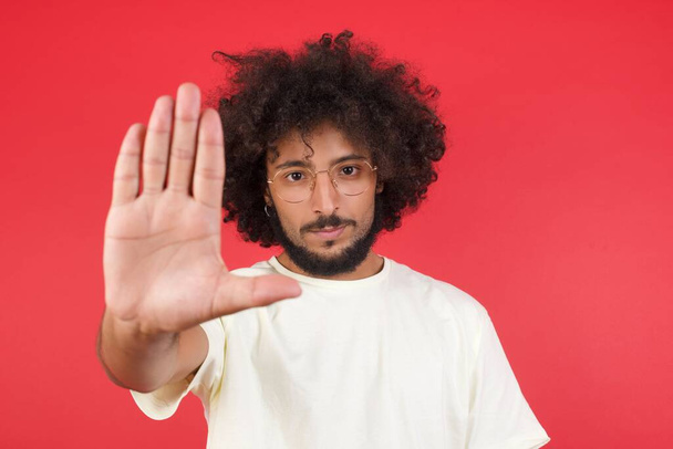 Nuori mies afro hiukset osoittaa stop vastaan punainen seinä  - Valokuva, kuva