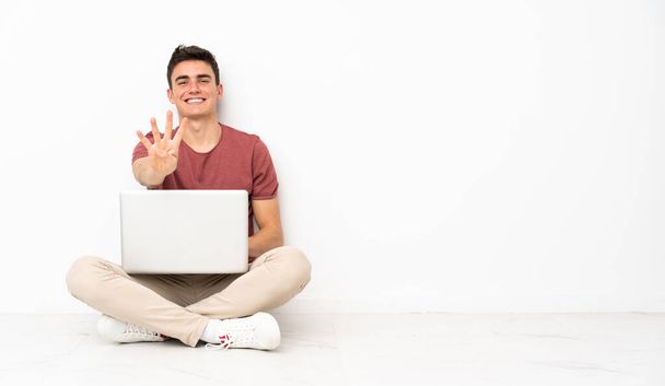Nastolatek siedzi na krześle ze swoim laptopem szczęśliwy i liczy cztery palce - Zdjęcie, obraz