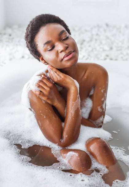 Pleasure and cleanliness. African american girl with closed eyes takes bath with foam - Photo, Image