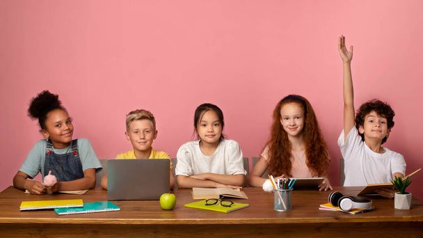 Slimme blanke jongen en zijn vrienden klaar om les te beantwoorden aan tafel tegen roze achtergrond, kopieer ruimte - Foto, afbeelding