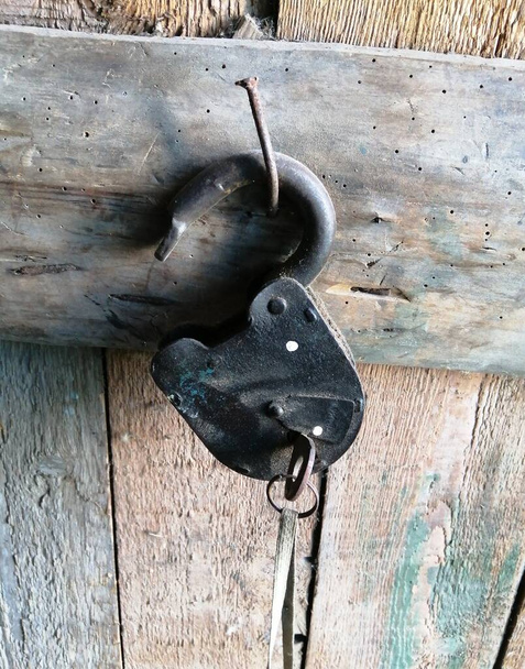 An old barn lock with keys, in a wooden shed, hanging from a large nail. Close-up photo. - Photo, Image