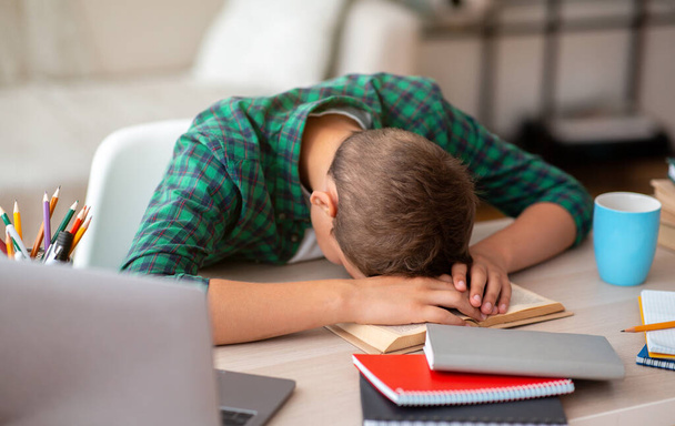 Müder Schuljunge schläft am Schreibtisch, während er Hausaufgaben macht - Foto, Bild