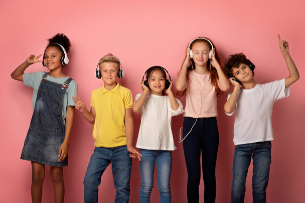 Alumnos multinacionales en auriculares disfrutando de música o escuchando audiolibros sobre fondo rosa - Foto, Imagen