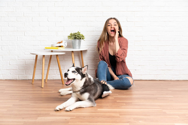 Young girl with her dog sitting in the floor at indoors shouting with mouth wide open - Фото, зображення