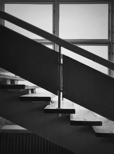 Siyah beyaz iç mimari detayları, pencerenin yanındaki eski merdivenler. Ahşap korkuluklar ve eski püskü bir binanın içindeki taş merdivenler. Yaşlanmış yapı elementleri. Dikey fotoğraf. - Fotoğraf, Görsel