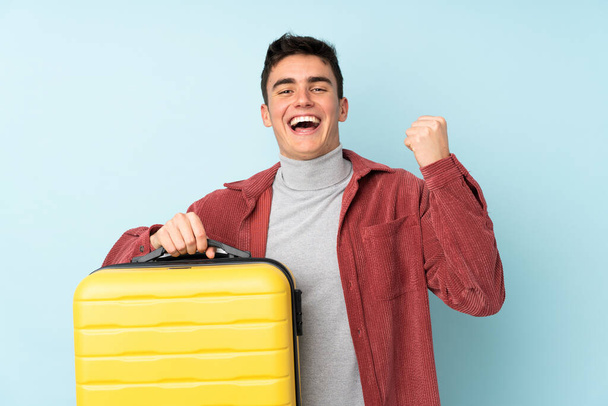 Teenager caucasian man isolated on purple background in vacation with travel suitcase - Valokuva, kuva