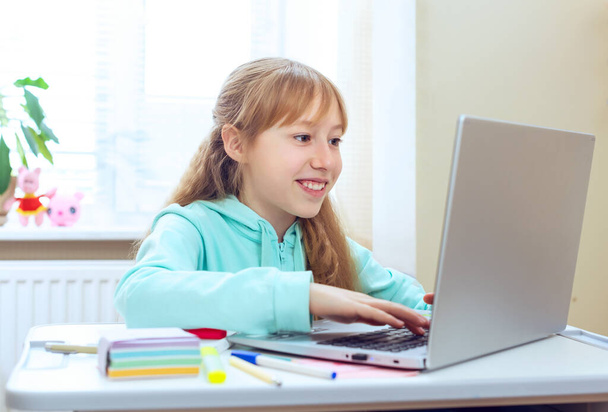 Nastolatka odrabiająca lekcje za pomocą komputera siedzącego przy biurku w pokoju, wpisująca na klawiaturze. Komunikacja z laptopem. Przytulne miejsce pracy, kształcenie na odległość, koncepcja e-learningu, nauka online - Zdjęcie, obraz