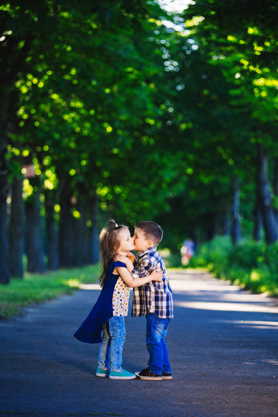 Gyermekszeretet, egy kisfiú és egy lány, szórakozás, nevetés és mosoly, és csók a szabadban. - Fotó, kép