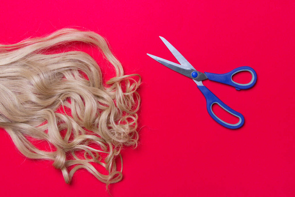 blond hair and scissors on red background, top view. - Photo, Image