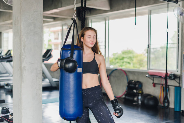 Female athletes punching sandbags To exercise in the gym. She wears black sportswear. And wear boxing gloves. - Foto, immagini