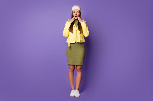 What Full size photo of pretty staring lady look shocked arms near mouth listen unexpected news wear yellow leather jacket green dress cap shoes isolated pastel purple color background - Foto, imagen