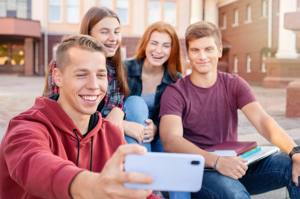Feliz grupo sonriente de estudiantes tomando fotos en el teléfono al aire libre cerca de la universidad. Concepto educativo - Foto, imagen