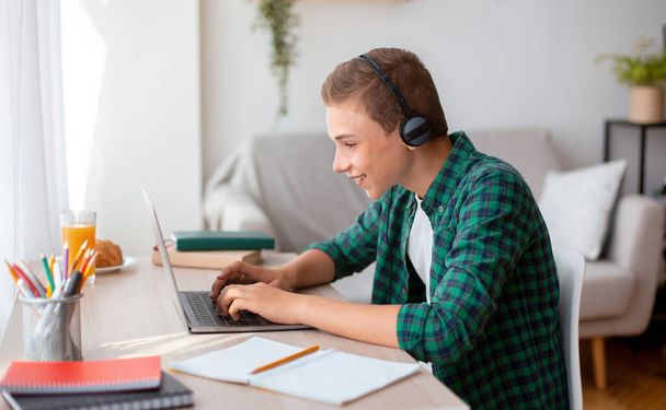 Cheerful schooler with headset typing on laptop - Photo, Image
