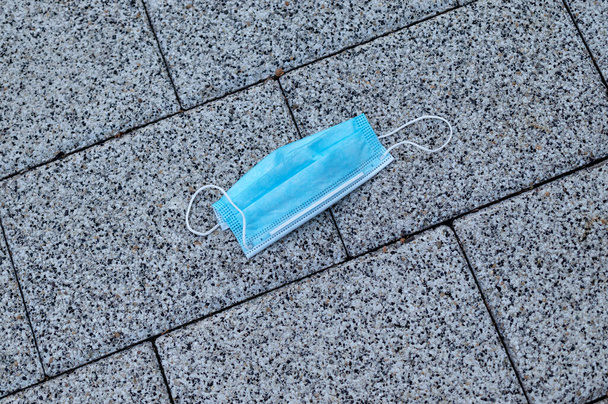 Ακατάλληλα πεταμένη μπλε μάσκα προσώπου πεταμένη μετά τη χρήση στο μονοπάτι του δρόμου. COVID-19 έννοια αποβλήτων ή απορριμμάτων. - Φωτογραφία, εικόνα