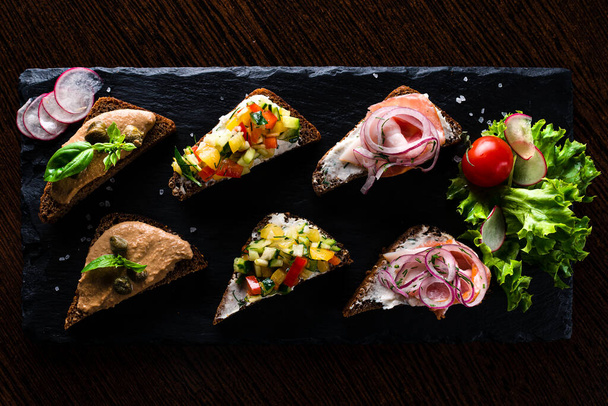 set of bruschetta on a tray, Set of mini sandwiches on black stone background, top view. - 写真・画像