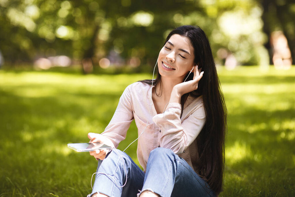 Relaxé asiatique fille profiter de écouter de la musique sur Smartphone en plein air, porter des écouteurs - Photo, image