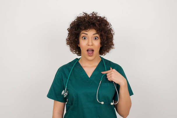 Překvapený krásný lékař žena je šokován, má užaslý výraz ukazuje na sebe s prstem  - Fotografie, Obrázek