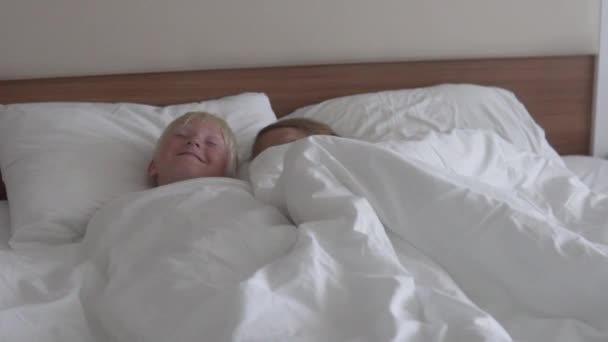 Cute children boy and girl rest in bed in a hotel room while on vacation - Materiał filmowy, wideo