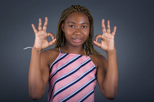 Glad young african american woman shows ok sign with both hands as expresses approval. Standing against gray wall. - Photo, Image