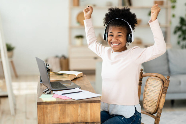 alegre negro chica en portátil sacudiendo puños aprendizaje en casa - Foto, Imagen