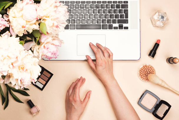 Блогер краси працює з ноутбуком, косметикою та квітами півоній на пастельному рожевому столі. Плоский прошарок, вид зверху
 - Фото, зображення