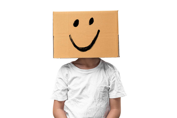 Klein meisje draagt kartonnen doos op zijn hoofd met smiley gezicht, geïsoleerd op witte achtergrond. - Foto, afbeelding