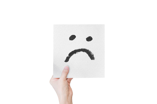Mano sosteniendo papel blanco con emoticonos faciales infelices dibujados a mano aislados sobre fondo blanco. con la ruta de recorte. - Foto, imagen