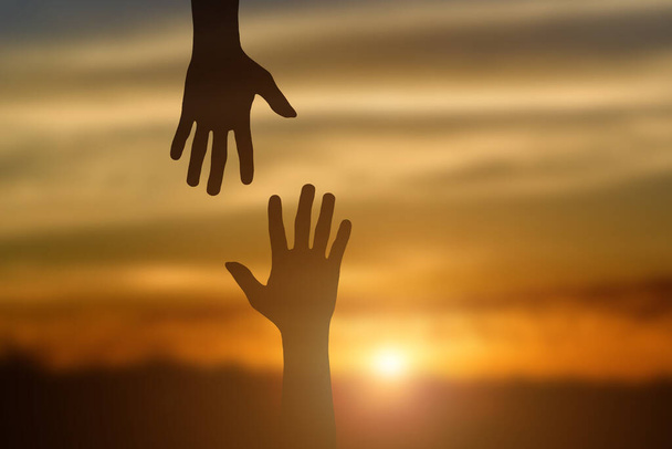 Silhouette des Gebens einer helfenden Hand, des Hoffens und der gegenseitigen Unterstützung über dem Hintergrund des Sonnenuntergangs. - Foto, Bild