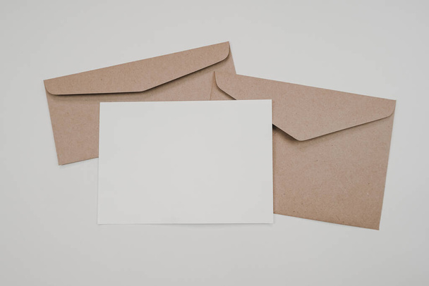 Blank white paper on the two brown paper envelope. Mock-up of horizontal blank greeting card. Top view of Craft paper envelope on white background. Flat lay of stationery. Minimalism style. - Φωτογραφία, εικόνα